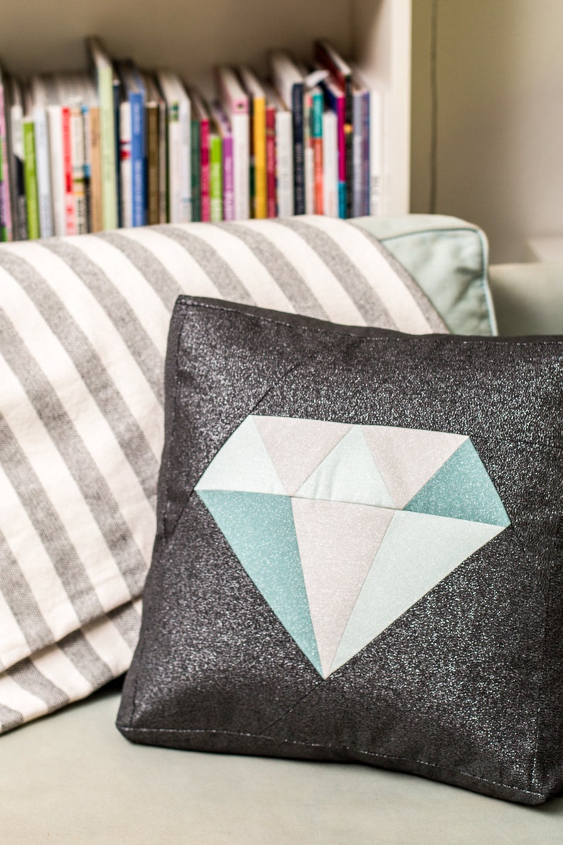 May include: A black pillow with a large diamond-shaped design in shades of blue and white. The diamond is made of fabric pieces sewn together.