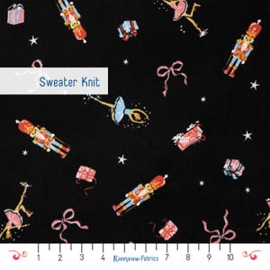 May include: Black sweater knit fabric featuring a repeating pattern of nutcrackers, ballerinas in blue and pink, gift boxes, and pink bows, interspersed with white stars. A ruler at the bottom shows measurements in inches from 1 to 10.