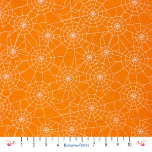 May include: Orange fabric with a repeating pattern of white spiderwebs. The spiderwebs are evenly spaced across the fabric, creating a Halloween-themed design. The fabric is marked with a ruler along the bottom edge.