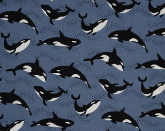 Op de afbeelding: Blauwe stof met een herhaald patroon van zwart-witte orka's. De walvissen staan in verschillende poses tegen een achtergrond met stippen. De tekst "Riverview Fabrics" is langs de onderkant gedrukt.