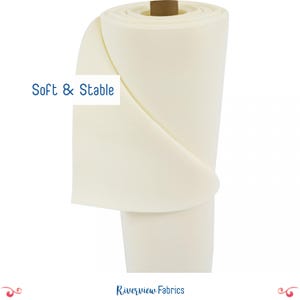May include: A roll of white, soft and stable fabric. The fabric is rolled up and tied with a brown ribbon. The text "Soft & Stable" is written in blue on a white background.