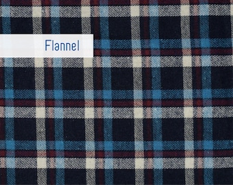 May include: Close-up of a fabric with a plaid pattern. The fabric features a navy blue base with intersecting lines of light blue, cream, and burgundy. The word "Flannel" is displayed on a white rectangle. The fabric is marked with inch measurements.