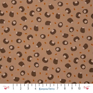 May include: Beige fabric featuring a repeating pattern of brown hedgehogs and small orange leaves. The hedgehogs have white faces and are scattered across the fabric. The fabric is marked with a ruler and the text "Riverview Fabrics".