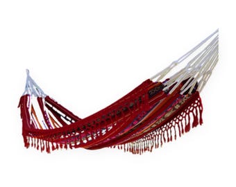 May include: A red hammock featuring woven patterns in shades of orange, purple, and white. The fabric body includes decorative fringe along the bottom edge and is suspended by thick white braided ropes at both ends for secure attachment.