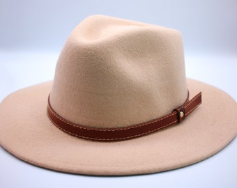 May include: A beige fedora hat with a brown leather band and a gold buckle. The hat has a wide brim and a slightly indented crown.