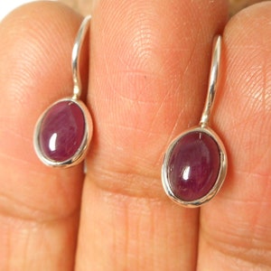 Könnte beinhalten: Ein Paar silberne Ohrringe mit kleinen ovalen roten Edelsteinen.