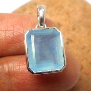 Könnte beinhalten: Ein silberner Anhänger mit einem hellblauen Edelstein, der in eine quadratische Form gefasst ist.