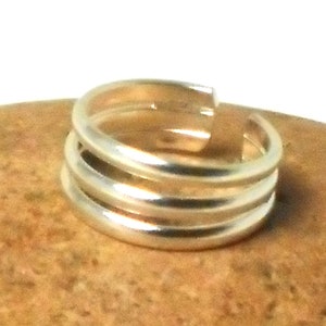 Peut inclure: Une bague en argent avec trois bandes empilées les unes sur les autres. La bague est sur une surface brune.