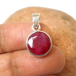 May include: A round red ruby gemstone pendant set in sterling silver. The pendant is on a white background.
