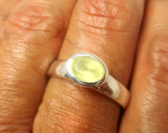 May include: A silver ring with a light yellow oval gemstone. The ring is on a finger, with the hand in the foreground. The ring's band is smooth and polished.