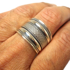 May include: A silver ring with a wide band and a textured design. The ring has three bands, each with a different pattern.
