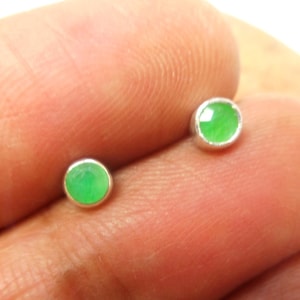 May include: A pair of silver stud earrings with small, round, green gemstones.