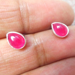 May include: A pair of silver stud earrings with pink teardrop-shaped gemstones.