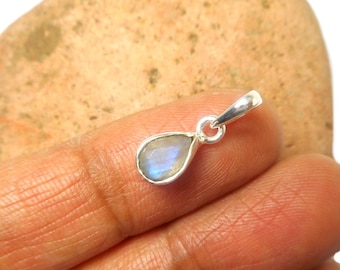 May include: A small teardrop-shaped pendant featuring a translucent, iridescent moonstone set in a polished silver-toned metal frame with a circular bail at the top for attachment to a chain or cord, showcasing a subtle blue light reflection.
