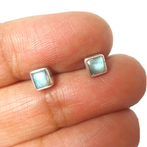 May include: Square stud earrings with a silver setting. The earrings have a light blue and green iridescent stone. These small, delicate earrings are suitable for everyday wear.