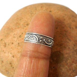 May include: A silver ring featuring a crescent moon and star design. The ring is worn on a finger.