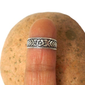 Könnte beinhalten: Ein silberner Ring mit einem floralen Design. Der Ring wird an einem Finger getragen.