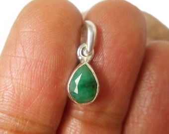 May include: A teardrop-shaped emerald pendant set in a polished silver bezel. The gemstone features a faceted surface with a deep green hue, suspended from a small silver bail at the top, designed for attachment to a necklace chain or cord.