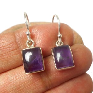 May include: A pair of silver dangle earrings featuring rectangular amethyst gemstones. The earrings have a simple design and are a classic choice for everyday wear.