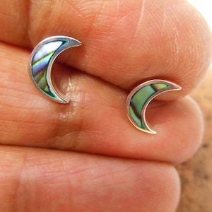 Pode incluir: Um par de brincos de prata em forma de lua crescente com incrustações de madrepérola de abalone. Os brincos têm um brilho iridescente verde, azul e roxo.