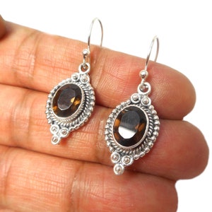 May include: Sterling silver earrings with a brown oval gemstone set in a detailed silver bezel. The earrings have a dangling design with a small silver bead at the bottom.