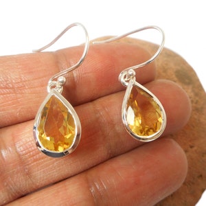 May include: A pair of silver teardrop earrings with yellow citrine gemstones.