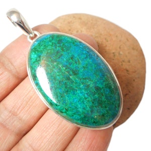 May include: A silver pendant featuring a large oval-shaped green and blue gemstone. The gemstone has a marbled pattern and a shiny, polished finish.
