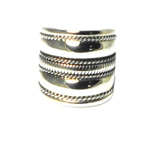 May include: A silver ring with a wide band and multiple decorative grooves.