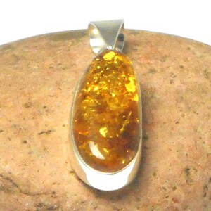 May include: A teardrop-shaped amber pendant set in a silver bezel. The amber is a rich, golden color with flecks of brown and yellow.