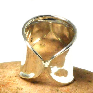 May include: A silver ring with a unique twisted design. The ring is wide and has a smooth, polished finish.
