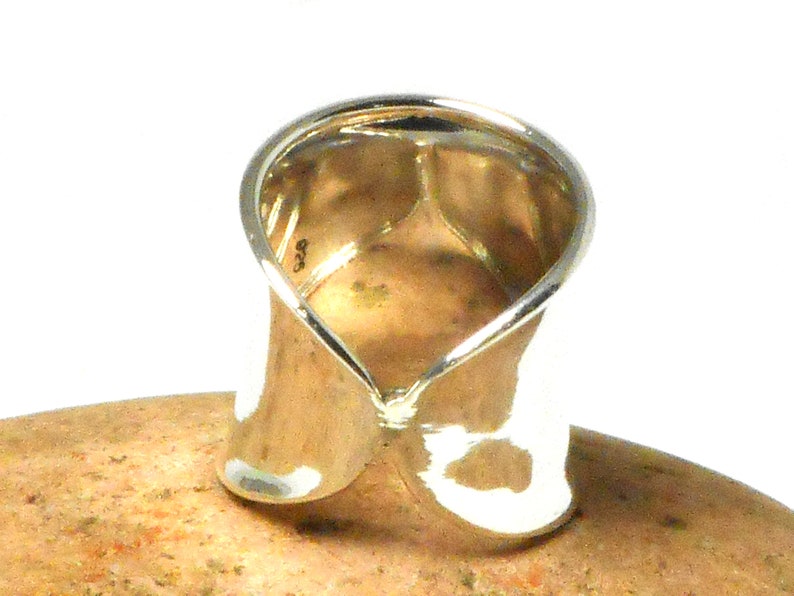 May include: A silver ring with a unique twisted design. The ring is wide and has a smooth, polished finish.