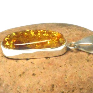 May include: A silver pendant with a large oval amber stone. The amber is a warm honey color with flecks of gold throughout.