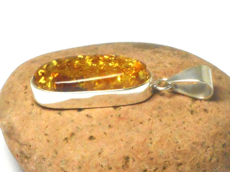 May include: A silver pendant with a large oval amber stone. The amber is a warm honey color with flecks of gold throughout.