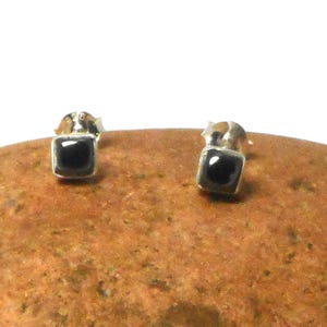 Könnte beinhalten: Ein Paar silberne Ohrstecker mit kleinen quadratischen schwarzen Onyxsteinen.