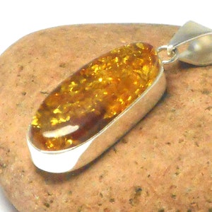May include: A silver pendant with a large oval amber stone. The amber is a deep yellow color with flecks of gold throughout. The pendant is on a brown rock.