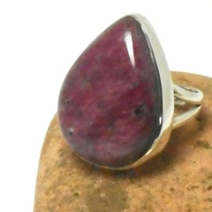 May include: A teardrop-shaped ring with a deep pink gemstone set in a silver band.
