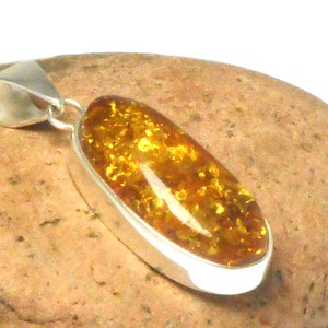 May include: A silver pendant with a large oval amber stone. The amber is a deep yellow color with flecks of gold throughout.