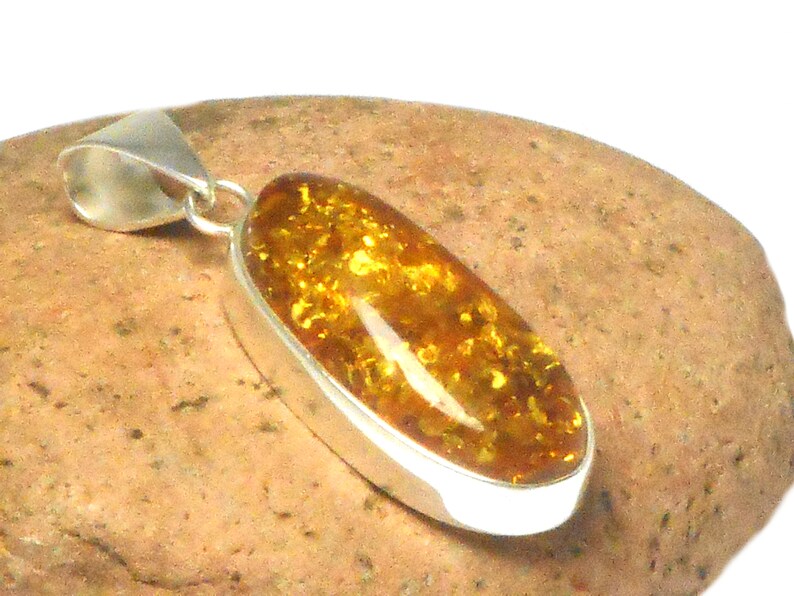 May include: A silver pendant with a large oval amber stone. The amber is a deep yellow color with flecks of gold throughout.