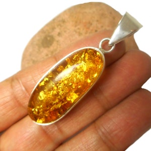 May include: A silver pendant with a large oval amber stone. The amber is a deep yellow color and has a lot of inclusions. The pendant is about 2 inches long.