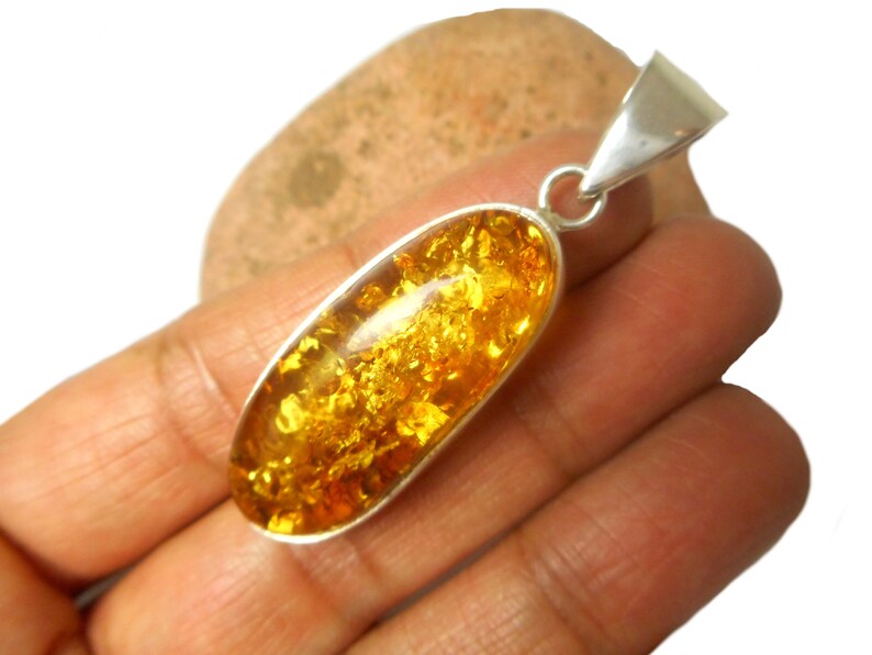 May include: A silver pendant with a large oval amber stone. The amber is a deep yellow color and has a lot of inclusions. The pendant is about 2 inches long.