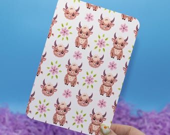May include: A rectangular card with a repeating pattern of cartoon Highland cows and pink flowers on a white background. The cows are brown with black horns and are in various poses. The card is held against a blue background.