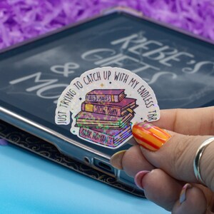 May include: A holographic sticker with a stack of books and the text "Just trying to catch up with my endless TBR".
