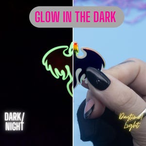 May include: A black and blue enamel pin with a glow-in-the-dark design of a bird. The pin is shown in both daylight and dark conditions, highlighting its glow-in-the-dark feature. "Glow in the Dark" and "Daytime Light" are written on the image.