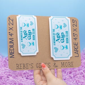 May include: Two rectangular stickers with a light blue border and text that reads "A MEMBER OF THE Age Gap BOOK CLUB". The stickers are on a brown cardboard backing. The medium sticker is 4' x 2.2' and the large sticker is 4.5' x 2.5'.