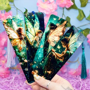 Puede incluir: Cuatro marcapáginas coloridos con ilustraciones de hadas con alas brillantes y un fondo verde y azul. Cada marcapáginas tiene un borla.