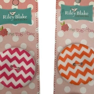 May include: Two round buttons with a chevron pattern. The button on the left is pink and white, and the button on the right is orange and white. Both buttons have the text "Sew Together" on the packaging.