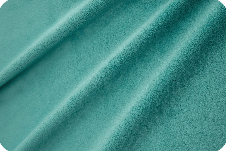 May include: A close-up of a soft, teal-coloured fabric with a smooth, velvety texture. The fabric is folded in a way that shows its drape and texture.
