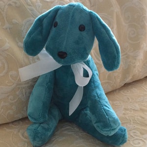 May include: A teal blue plush toy dog with a white ribbon around its neck. The dog has black eyes and a black nose.