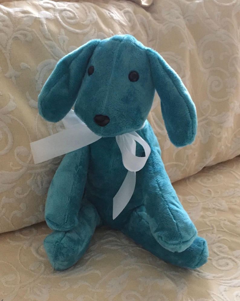 May include: A teal blue plush toy dog with a white ribbon around its neck. The dog has black eyes and a black nose.