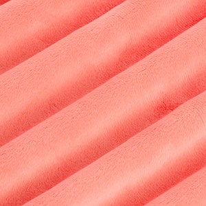 Puede incluir: Primer plano de una tela suave de color coral con textura peluda. La tela est&aacute; doblada en un patr&oacute;n ondulado, creando un aspecto suave y fluido.